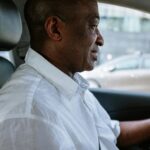 African American man driving a vehicle wearing a white shirt. Urban transportation scene.